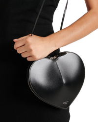 Alaïa Le Coeur leather shoulder bag in black on model, close-up of the sculpted heart shape held by its slim strap
