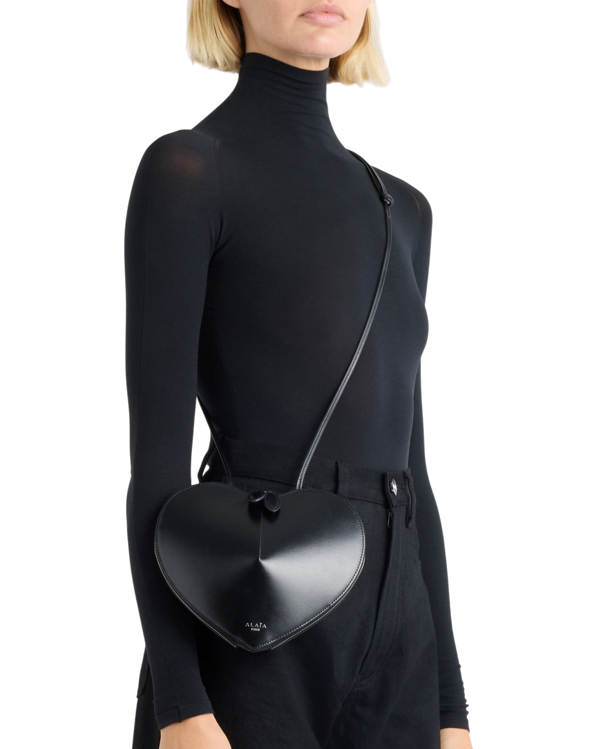 Alaïa Le Coeur leather shoulder bag in black on model, worn crossbody on a thin strap over a black turtleneck