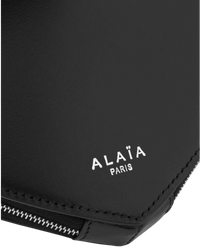 Alaïa Le Coeur leather shoulder bag in black, detail close-up of the white Alaïa Paris logo and zipper edge