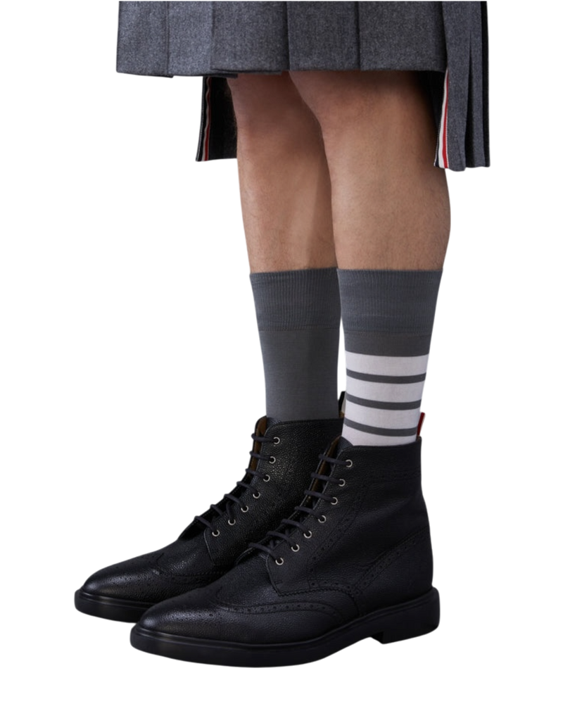 Thom Browne pebbled leather boots in black on model, worn with grey four-bar socks and a pleated grey kilt