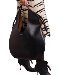 Loewe Paseo knotted leather tote in black on model, carried by the top handle with knotted cord ends at each side