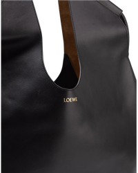 Detail of the gold-stamped LOEWE house mark on the front of the black leather tote, beside the tan suede handle lining